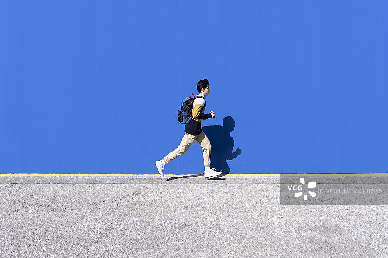背着背包在墙边奔跑的青少年图片素材