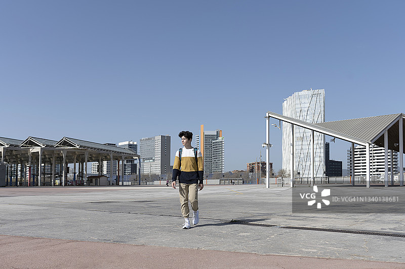 在阳光明媚的城市里背包行走的年轻男子正面照图片素材