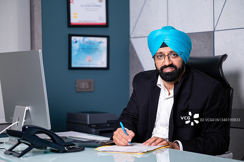 坐在办公室桌子旁进行会计核算的中年锡克教商人图片素材