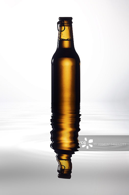 白色背景上的玻璃啤酒瓶，在水面上的倒影图片素材