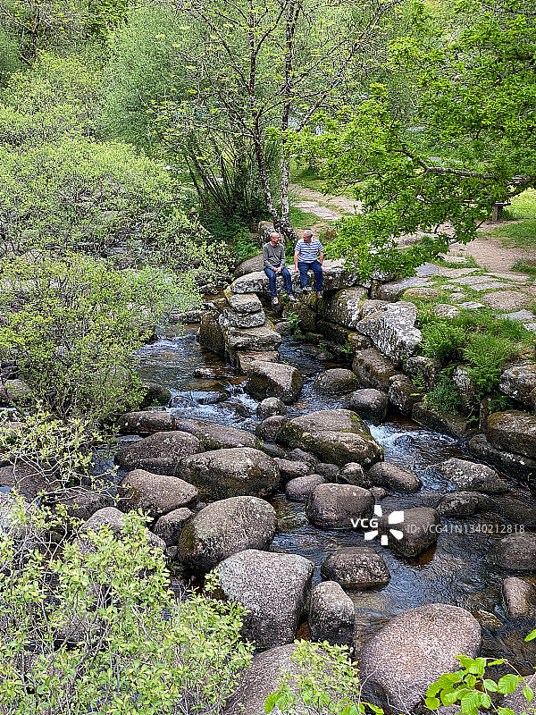 两名男子坐在河边的岩石上图片素材