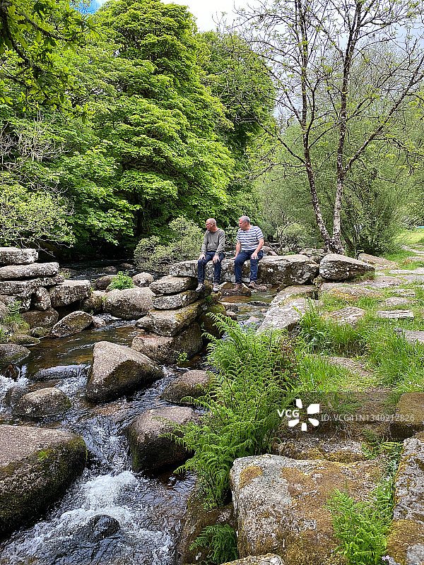 两名男子坐在河边的岩石上图片素材