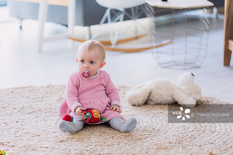可爱的女婴坐在客厅的地毯上抱着她的玩具图片素材