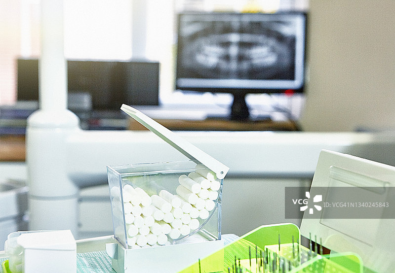 牙科诊所场景：牙钻头、吸水棉卷和显示牙科X光片的电脑图片素材