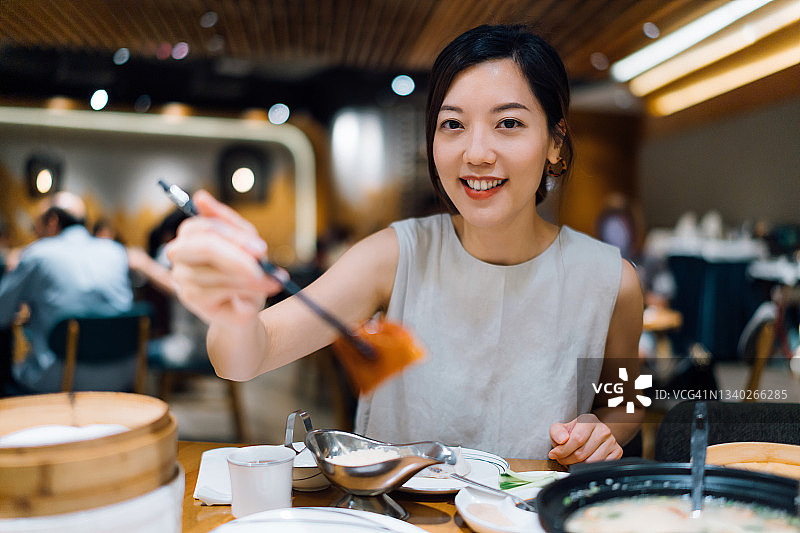 美丽的年轻亚洲女性对着镜头微笑，品尝中国传统美食北京烤鸭，享受美食文化和生活图片素材