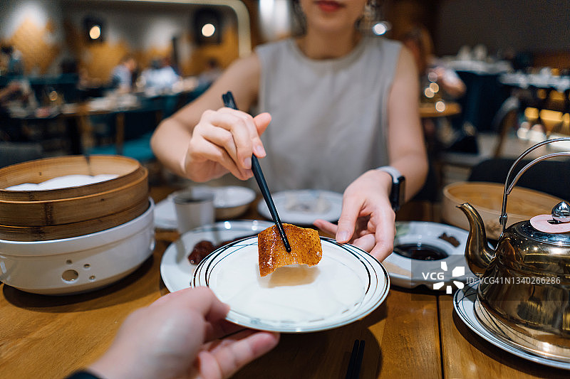 年轻的亚洲夫妇在中国餐馆享用传统中国菜肴——烤北京烤鸭的个人视角。女人正在为男人盘子里盛北京烤鸭。 传统的中国美食和饮食文化。外出就餐的生活方式图片素材