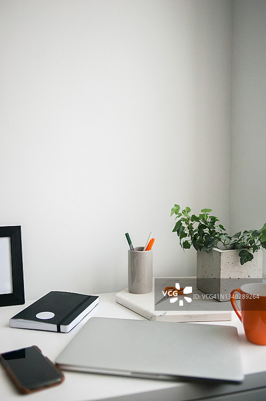 带有笔记本电脑、手机、黑色笔记本、橙色马克杯和其他物品的家庭工作场所。准备好在家工作。图片素材