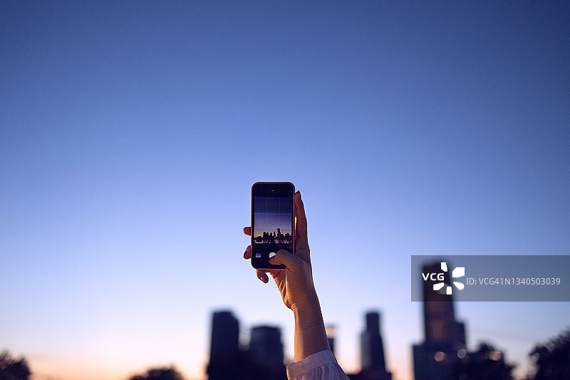 年轻女性用智能手机拍摄黄昏时分的现代城市景观图片素材