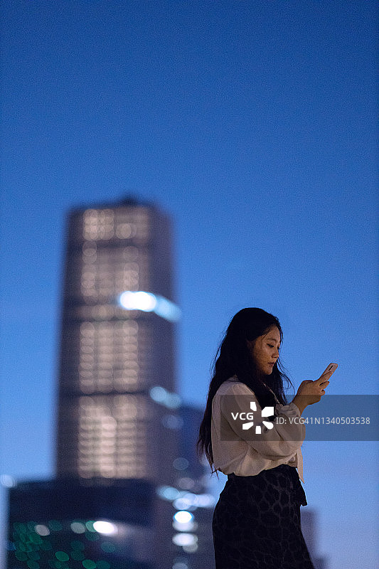 年轻女商人在上海市中心摩天大楼下使用智能手机图片素材