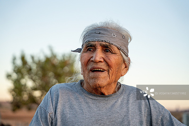 在犹他州或亚利桑那州纪念碑谷的后院里，在阳光明媚的午后对着镜头微笑的年长纳瓦霍美国原住民男人肖像图片素材