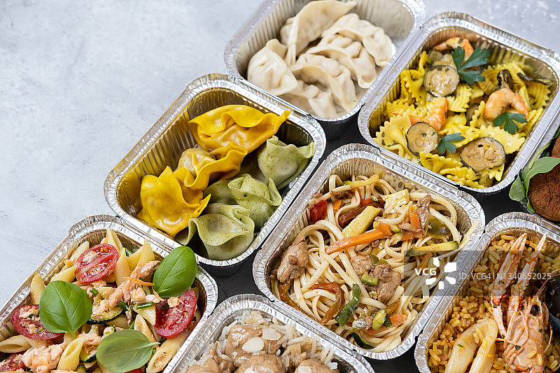 外卖配送：中式和意式外卖食品，含饺子、鸡肉面条、鸡肉米饭、三文鱼意面和炸豆丸子的铝制午餐盒图片素材