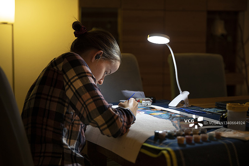 青少年在餐桌旁借台灯在晚上进行数字绘画图片素材