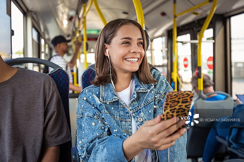 在公交车上使用手机的微笑女孩图片素材