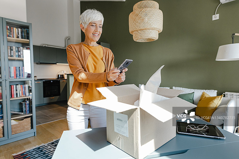 年长的女人打开包裹并拍摄网上订购的商品图片素材