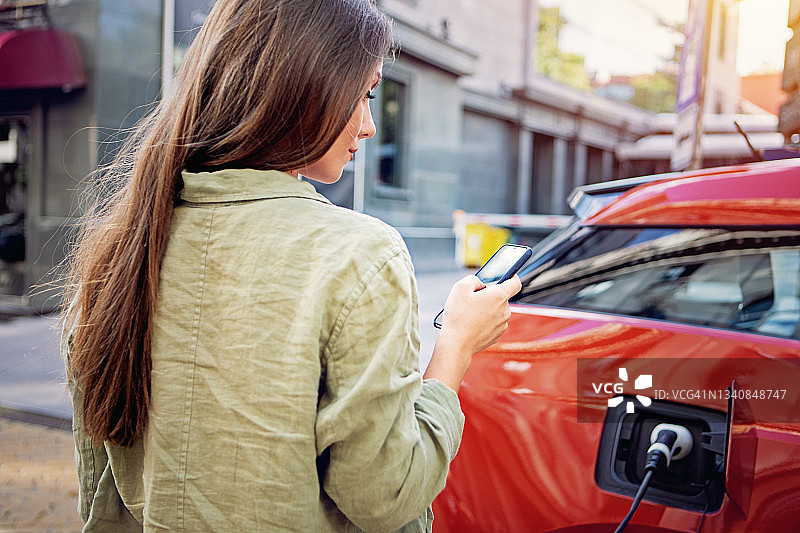 用手机为电动汽车充电的女子肖像图片素材
