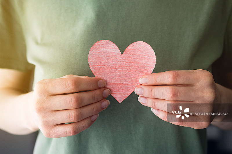 女人拿着红色纸质爱心或情人节卡片，背景为绿色休闲服装或T恤，情人节的概念，爱与忠诚的象征图片素材