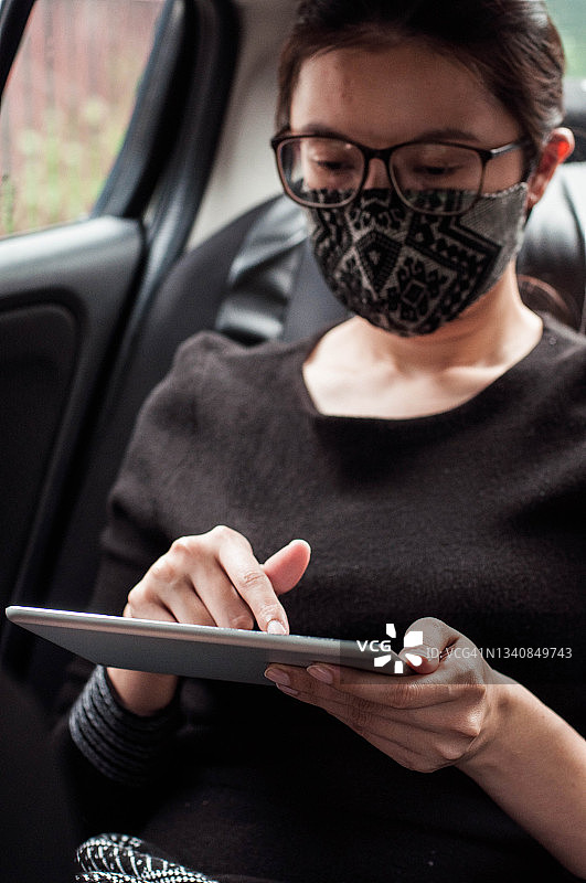 一位戴着防护面罩的年轻东南亚女性在车里使用数字平板电脑图片素材