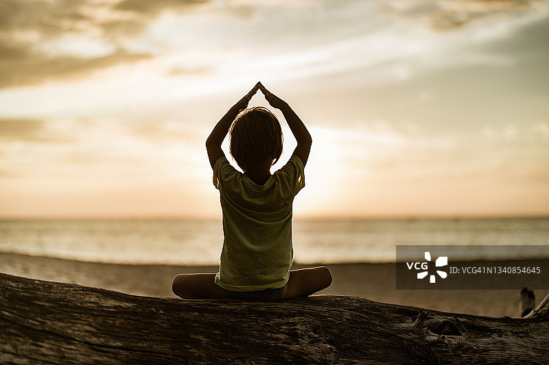 小男孩在日落时分的海滩上冥想图片素材