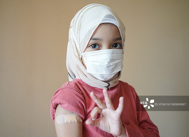 戴着口罩的亚洲穆斯林儿童患者在医院接受护士注射的冠状病毒或流感疫苗。疫苗接种、免疫接种、疾病预防理念。图片素材