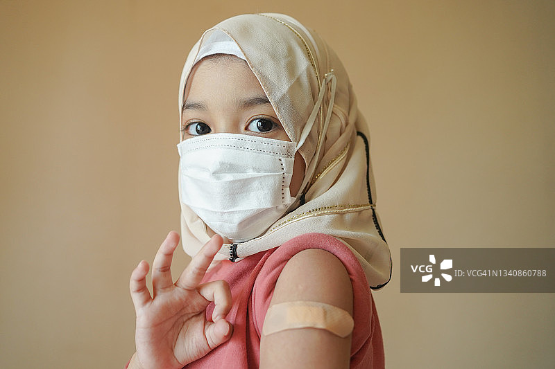 戴着口罩的亚洲穆斯林儿童在医院接受护士注射的冠状病毒或流感疫苗。疫苗接种、免疫、疾病预防概念。图片素材