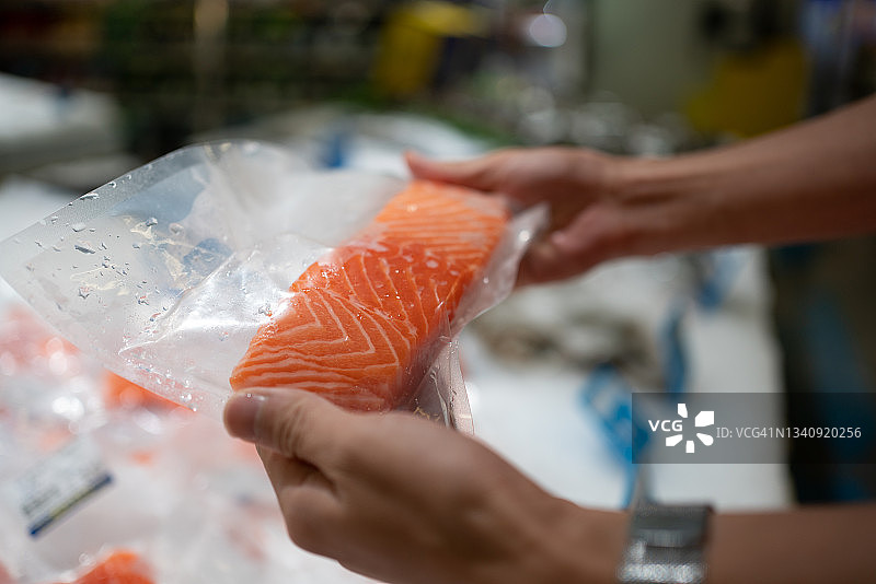 亚洲男人在超市购买三文鱼，手里拿着包装好的三文鱼图片素材