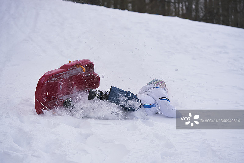 雪季里从红色雪橇上摔下来的男孩图片素材