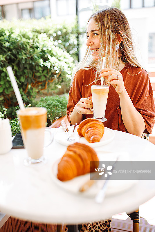 咖啡馆里的卡布奇诺和法式羊角面包，一位女士正在享用早餐图片素材