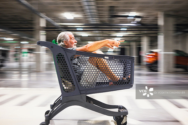坐在地下停车场移动购物车里的老人图片素材