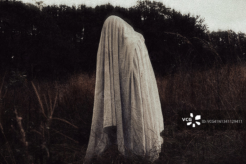 乡村背景下一个裹着床单的鬼魂恐怖概念，带有复古的编辑效果图片素材