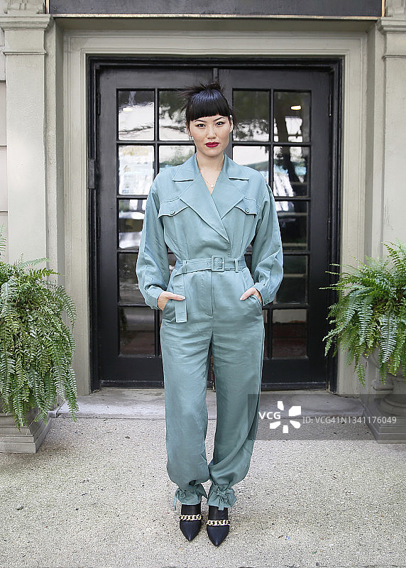 一位留着刘海的亚洲千禧一代女性的肖像，她坐在市中心，穿着绿色连体裤，面带微笑图片素材