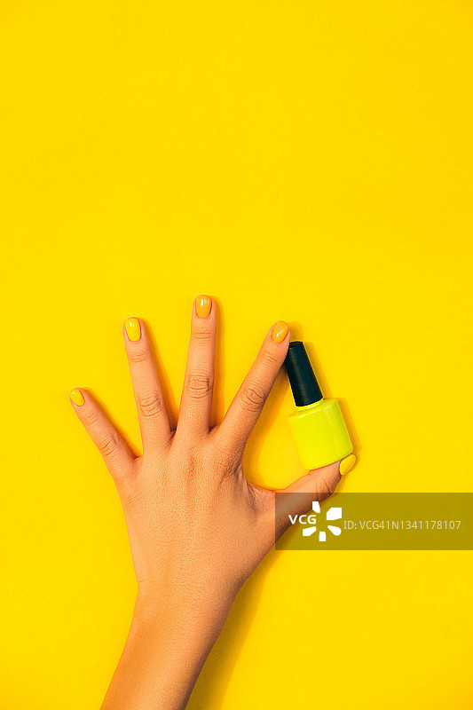 女人手持黄色指甲油，黄色背景。家庭生活理念。扁平风格。年度流行色图片素材