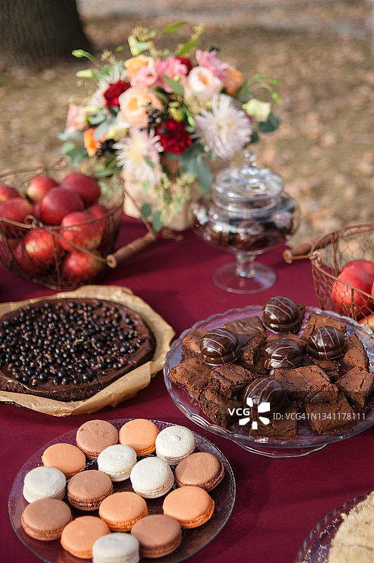 节日餐桌：甜点、自制布朗尼派、马卡龙、纸杯蛋糕、新鲜苹果和鲜花，Marsala色纺织桌布图片素材