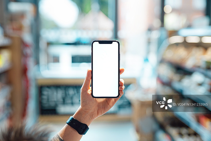 在超市里举着空白屏幕的智能手机图片素材