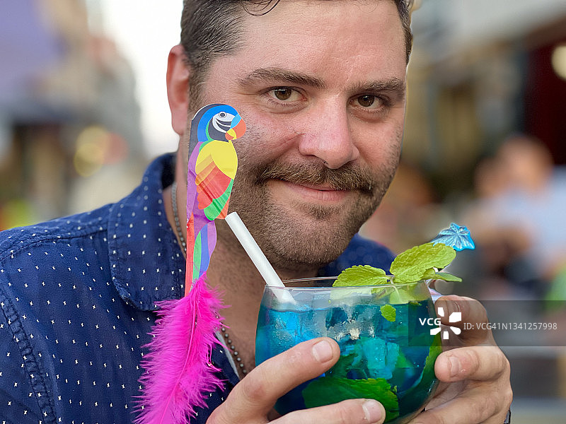 留着胡子的男人举着装饰有鹦鹉的节日热带夏季鸡尾酒图片素材