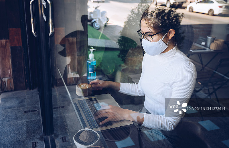 疫情期间在咖啡馆戴口罩使用笔记本电脑的亚洲女人图片素材
