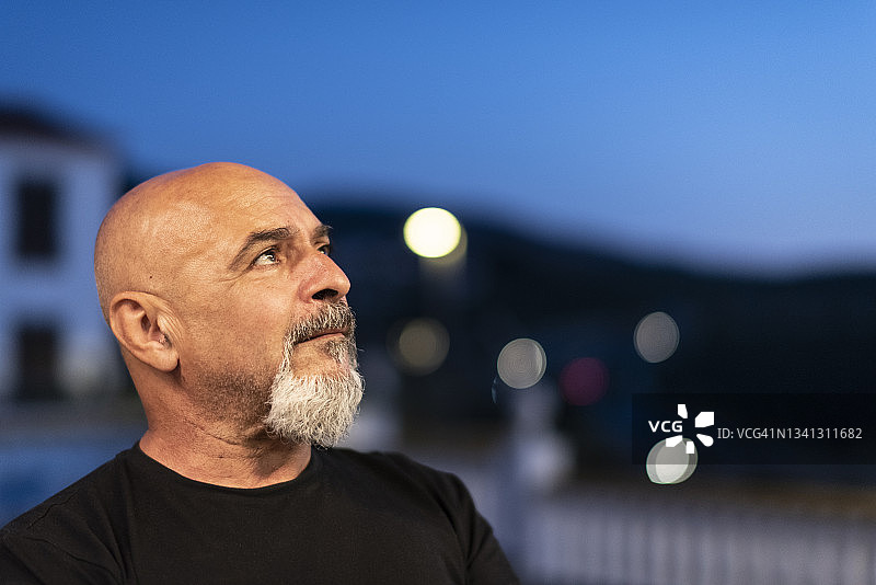 在蓝色时刻夜幕下，以交通灯为背景的60岁成熟男人图片素材