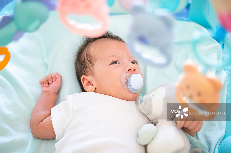 出生40天的新生男婴躺在床上，周围环绕着玩具图片素材
