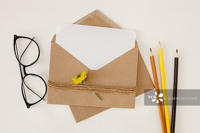 白色背景上的棕色手工纸信封、白色卡片、铅笔、眼镜和花图片素材
