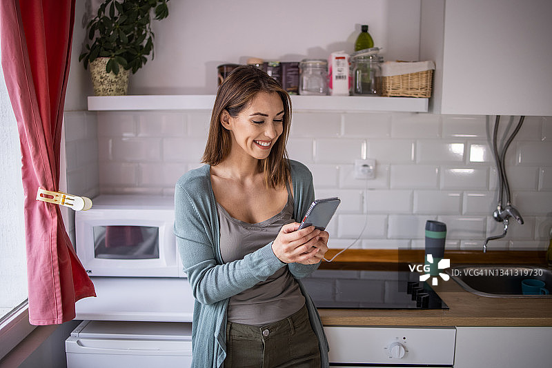 在厨房里使用手机的微笑女人图片素材