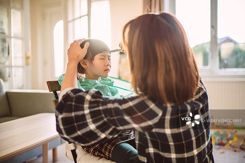 妈妈在家给可爱的小女儿剪头发图片素材