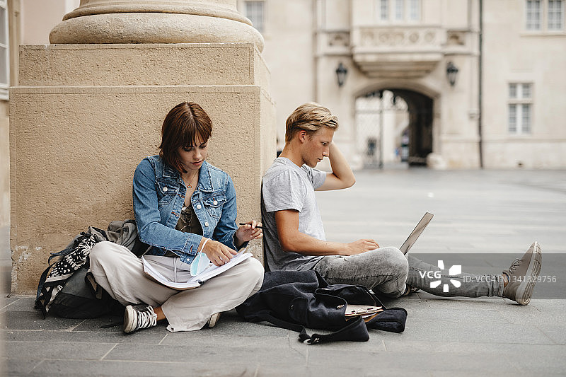 在校园里坐在地上用笔记本电脑学习的大学生图片素材
