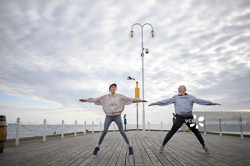 活跃的老年夫妇在清晨的海边码头上做开合跳运动图片素材
