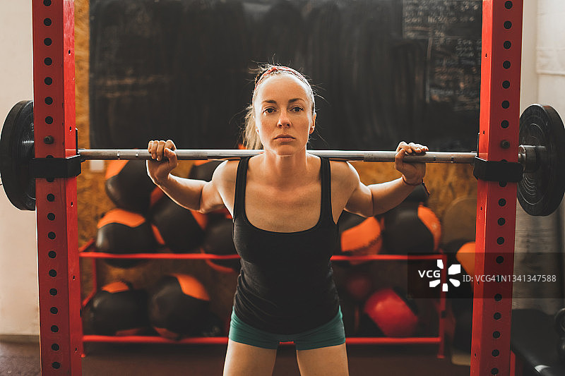 年轻女人握着杠铃，准备在健身房做过头深蹲图片素材