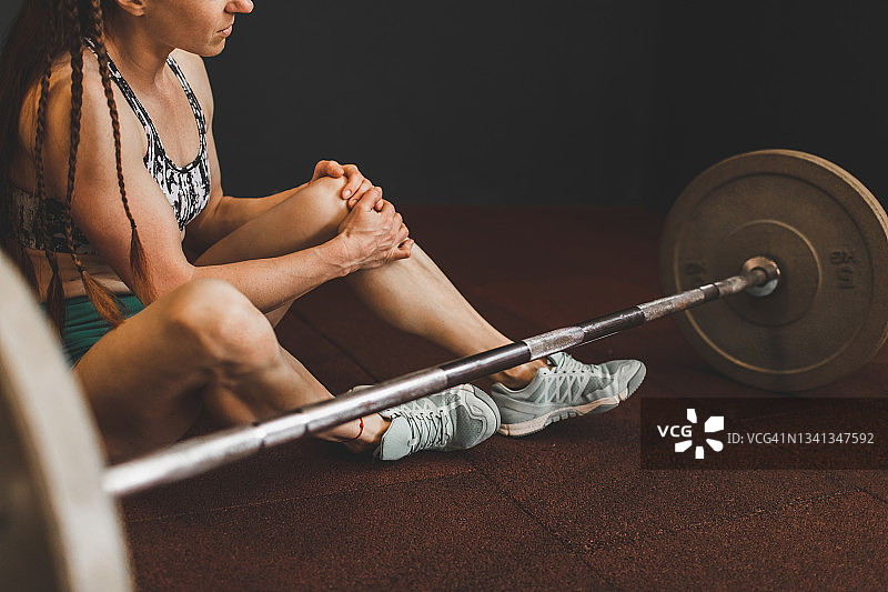 女性在健身房举杠铃时膝盖受伤：健康问题、韧带扭伤、压力和疼痛图片素材