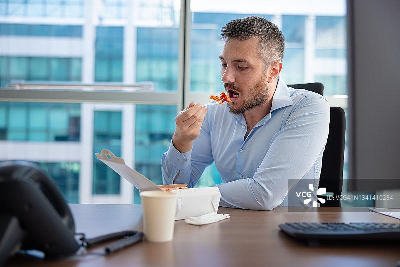 男人坐在办公室桌旁，在短暂的休息时间吃外卖图片素材