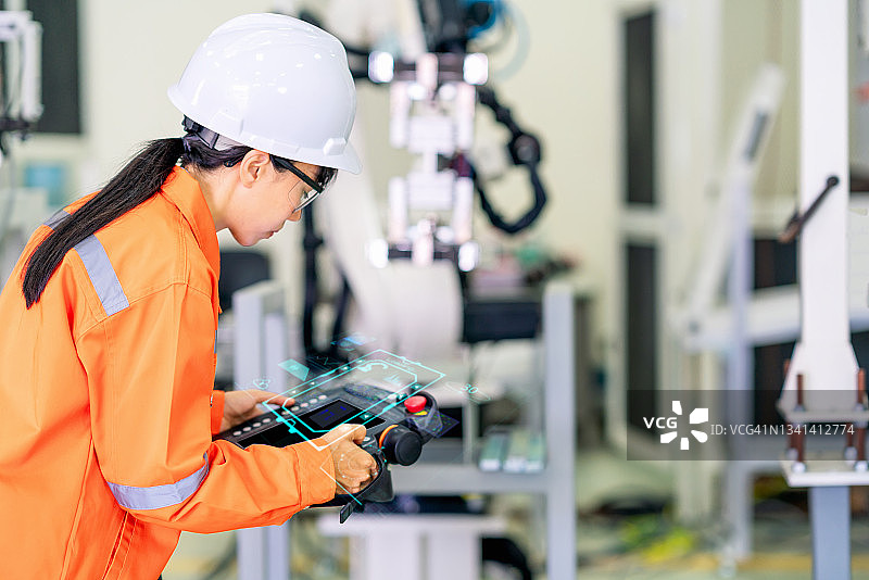 机器人教练在机器人手臂控制器上进行教学，观察数字显示器，用于金属板材的成型过程。现代工厂的工业制造过程由机器人控制。工厂4.0概念图片素材