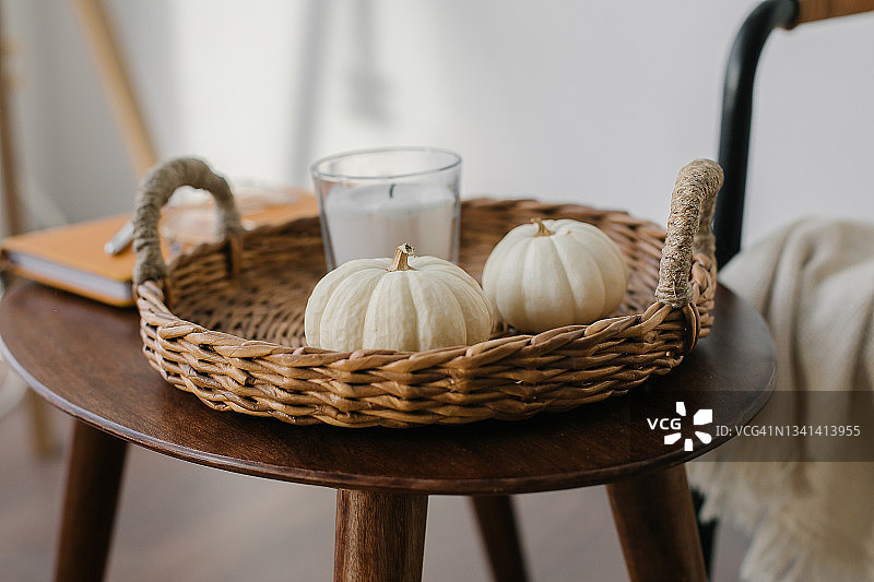 秋季静物：木桌草盘上的白色南瓜和燃烧的蜡烛，舒适秋季构图图片素材