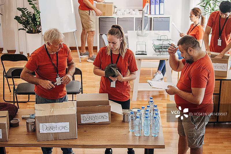 志愿者团队在捐赠中心分享和包装食物、衣服和水，用盒子装好送给有需要的人图片素材