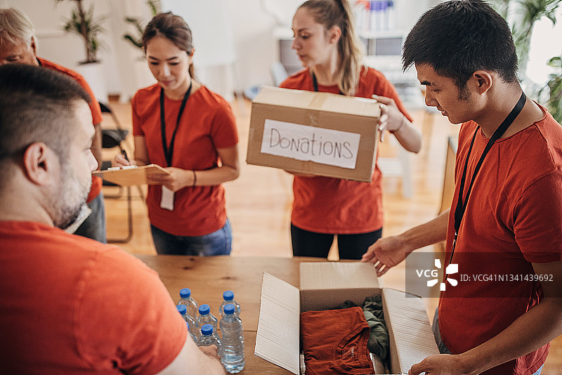 志愿者团队在捐赠中心分享和包装食物、衣服和水，用盒子装好送给有需要的人图片素材