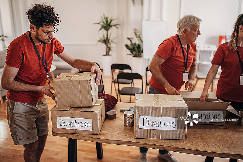 志愿者团队在捐赠中心分享和包装食物、衣服和水，用盒子装好送给有需要的人图片素材